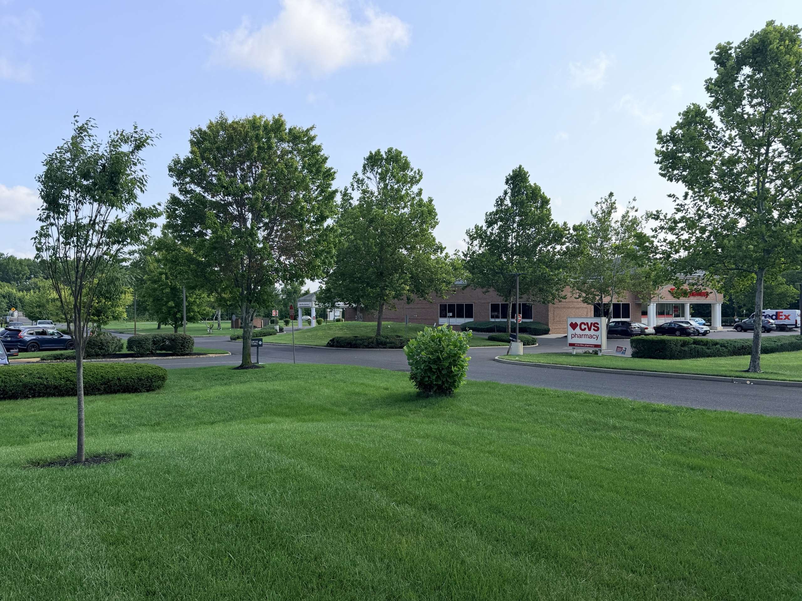 Sunlit parking lot in front of a CVS Pharmacy, with green trees and manicured lawn in the foreground.