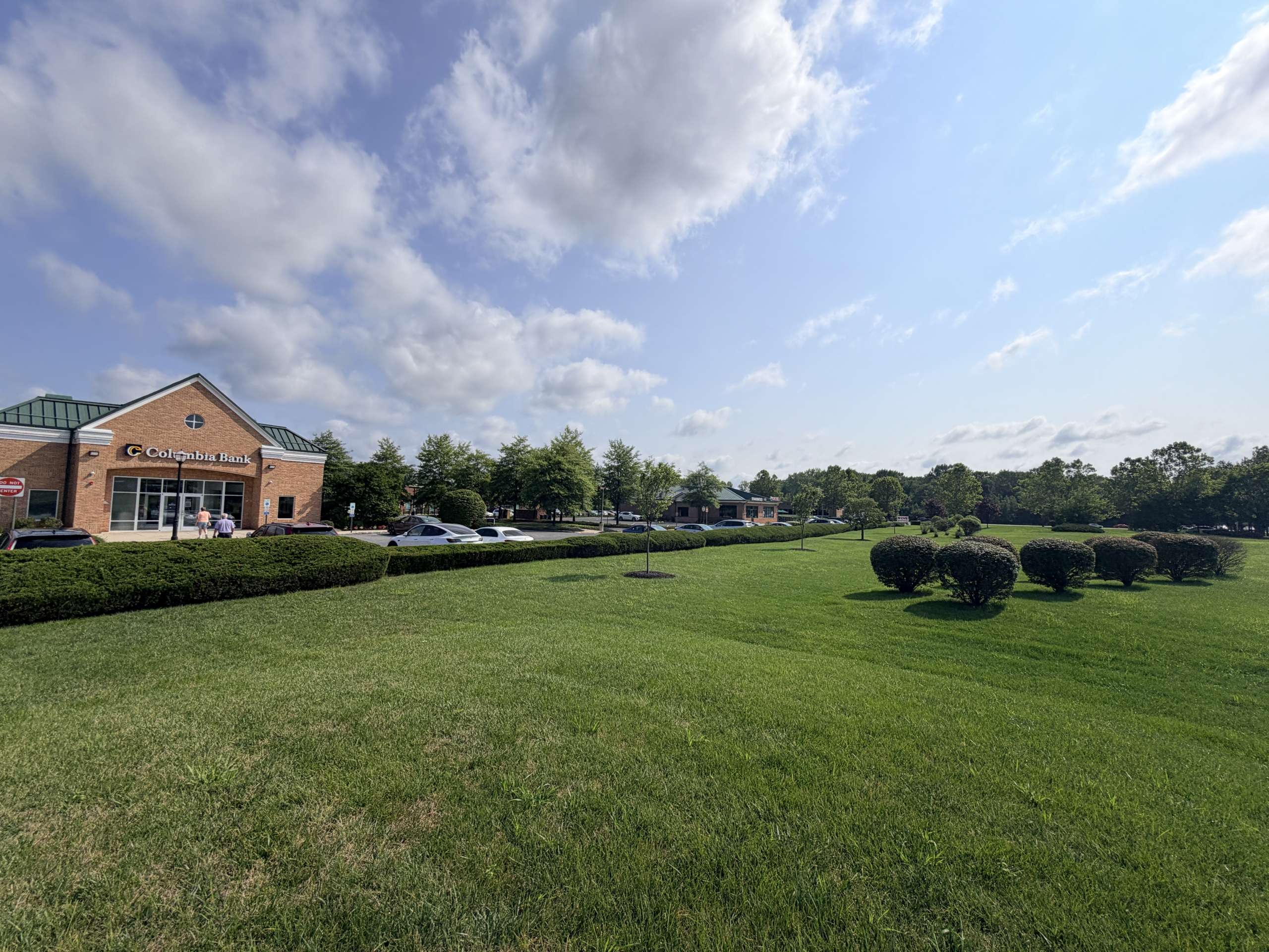 Brick Columbia Bank storefront with glass doors, cars in the lot, and a manicured lawn under a blue sky vs clouds.