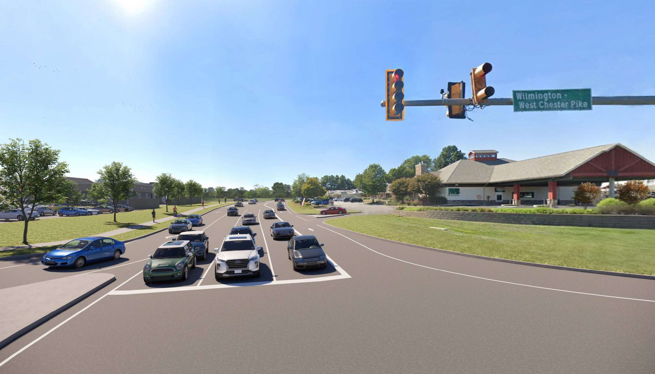 Multi-lane road at an intersection with a traffic light; a sign reads Wilmington West Chester Pike and a shopping center is on the right under a blue sky.