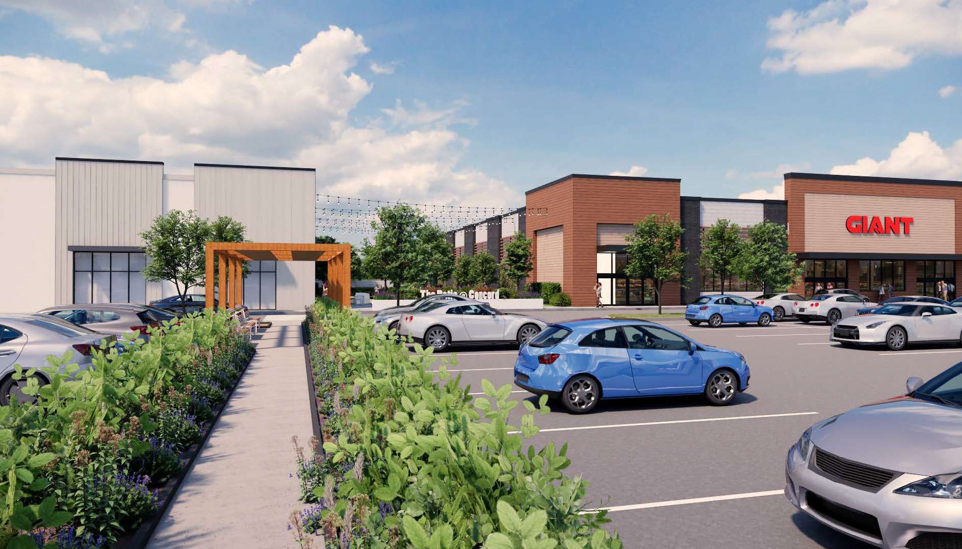 Parking lot of a shopping plaza with a Giant store, cars parked and greenery along a walkway under a blue sky with clouds.