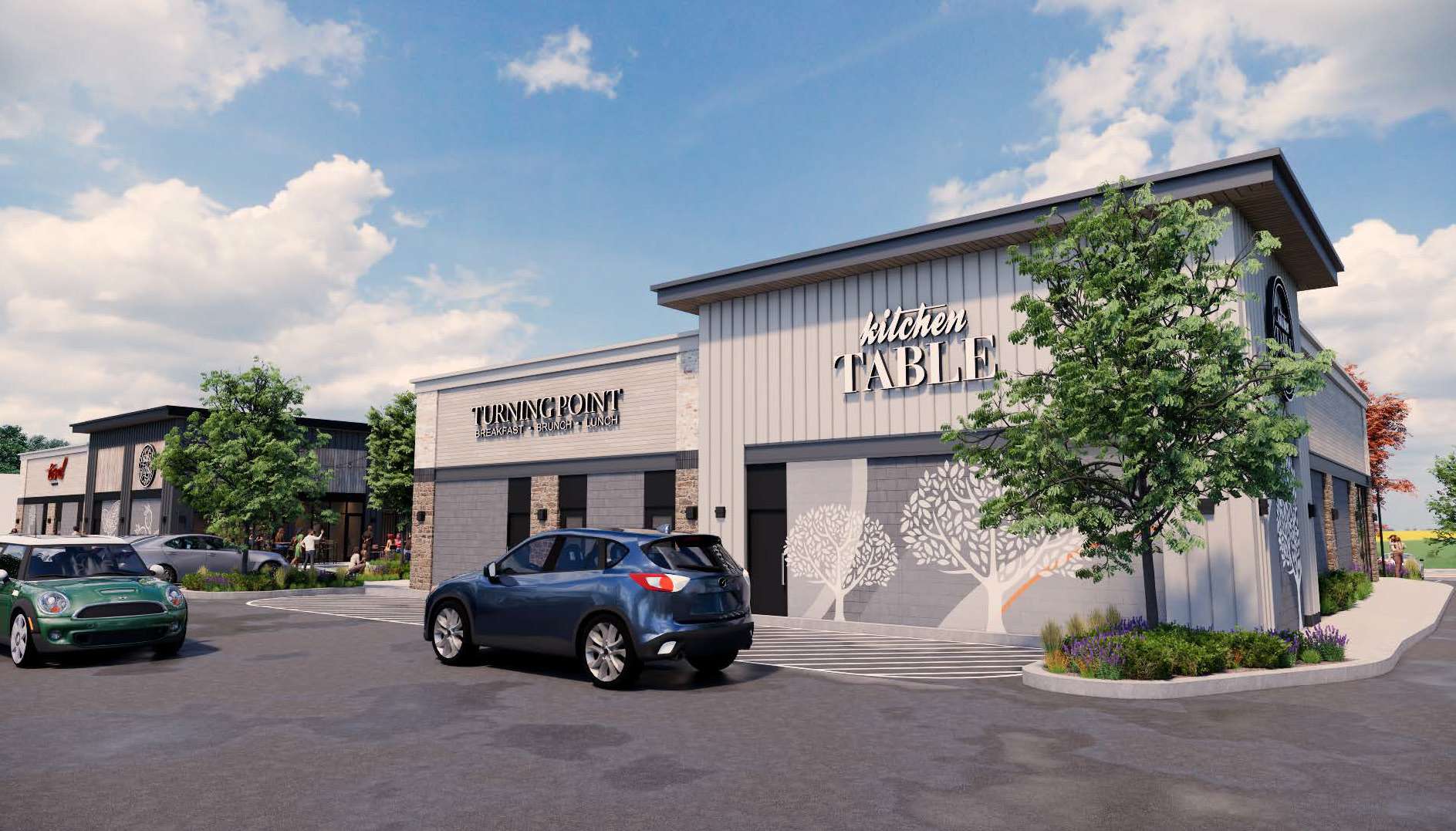 Exterior of a modern shopping plaza with Kitchen Table and Turning Point restaurant storefronts under a blue sky.