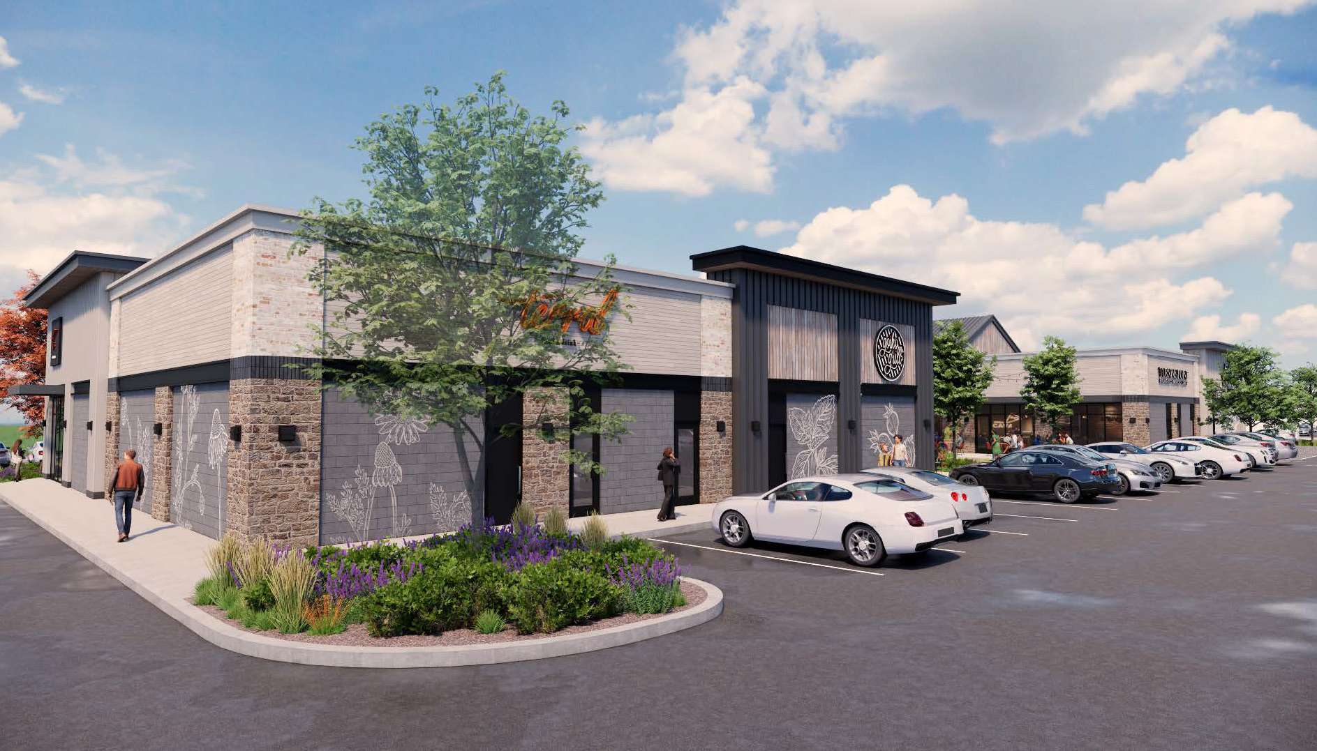 Modern retail complex with brick and stone facade, landscaped island in the foreground, and parked cars under a partly cloudy blue sky?