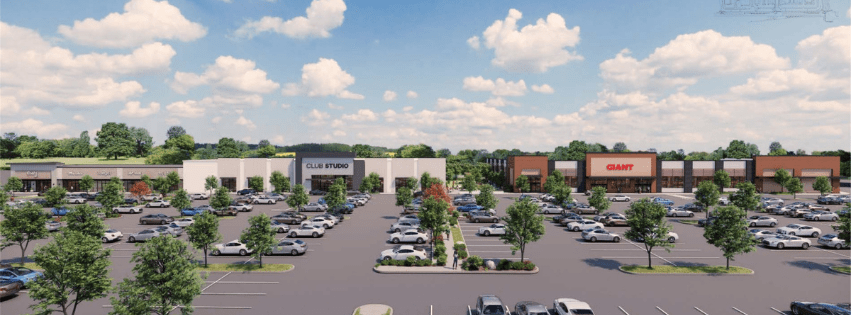 Outdoor shopping center with a wide parking lot and green trees, storefronts labeled Giant and Club Studio under a blue, partly cloudy sky
